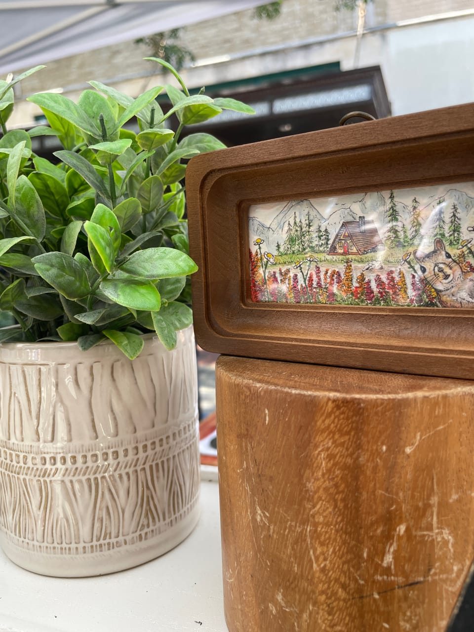 Photo of original tiny art and a wooden frame next to a potted plant